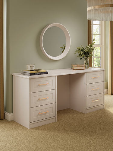 Lincoln double pedestal dressing table in cashmere with gold handles in a cozy care home bedroom. With books, a jewellery box and vase with fresh flowers on top of the dressing table. There is a mirror above the dressing table.