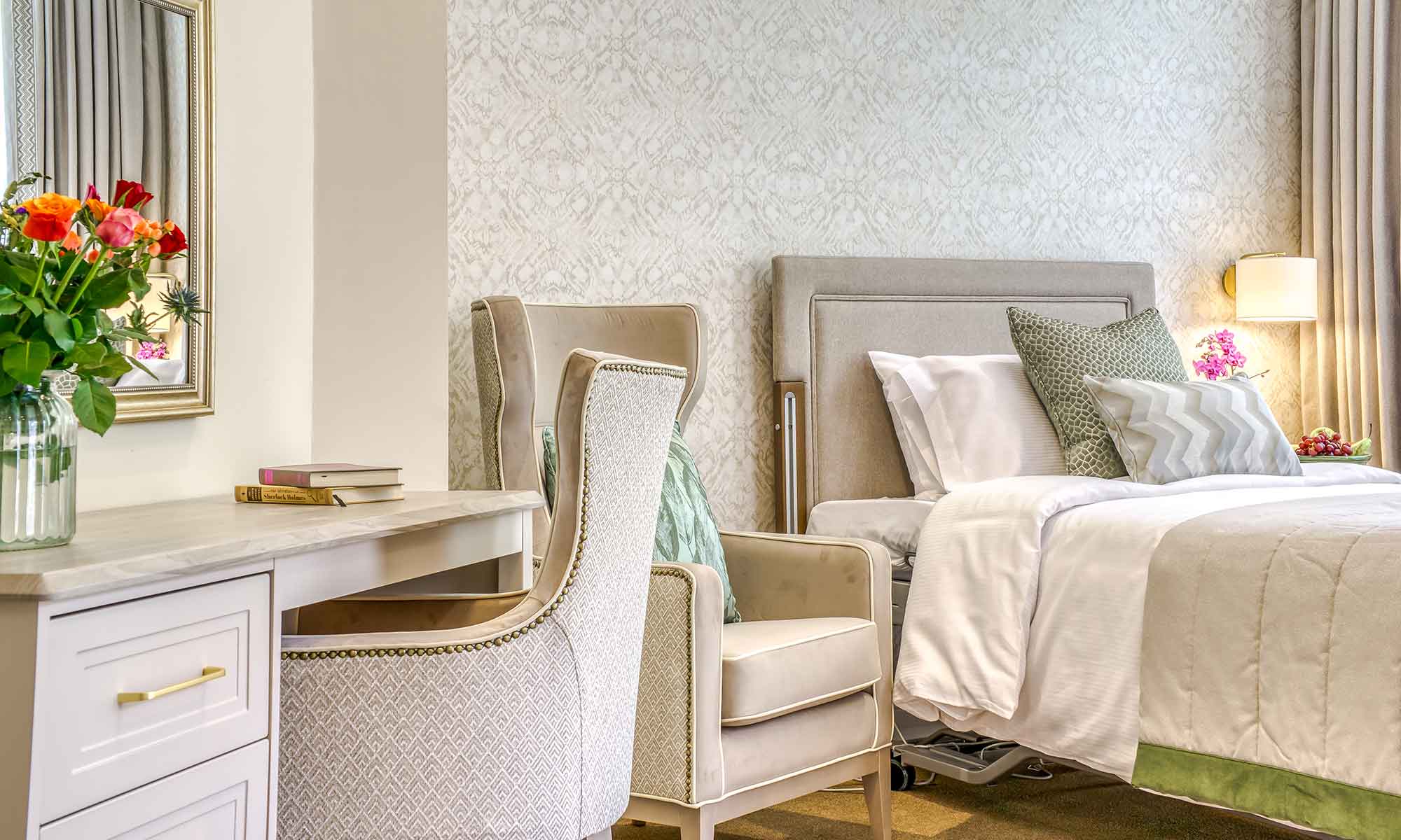 Elegant bedroom featuring a Valls wingback chair with intricate piping and studding detail, set against a dressing table with soft backlighting and tasteful decor elements, including fresh flowers and vase.