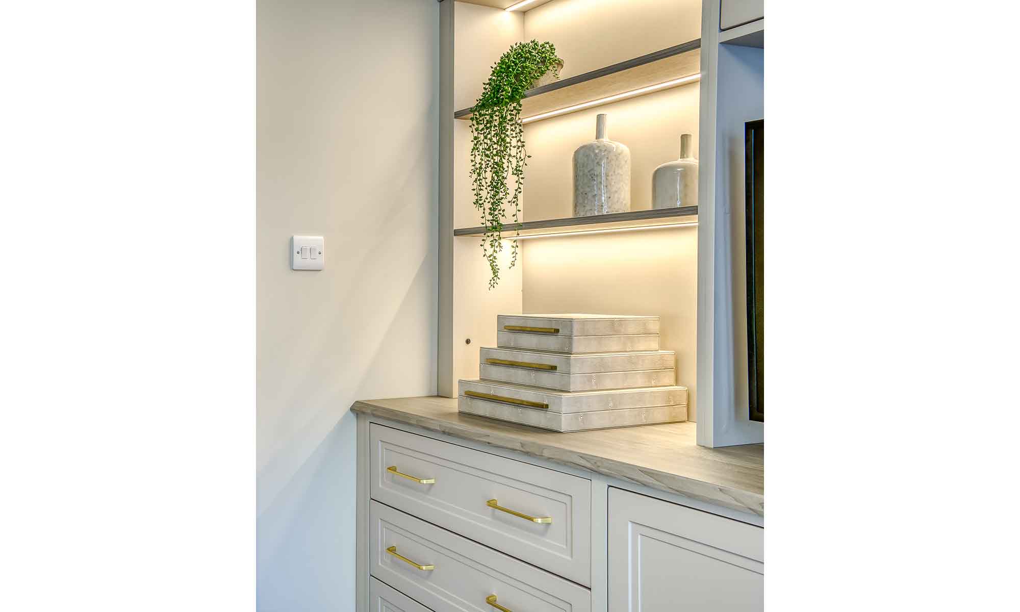 Bespoke fitted bedroom cabinetry showing open shelving with books and indoor plants placed on shelves.